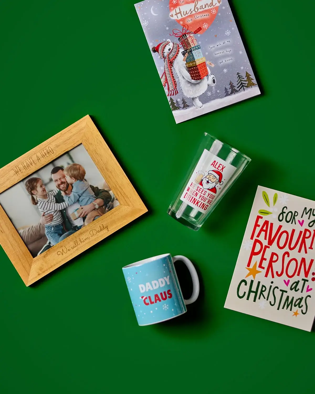 Christmas gift collection featuring greeting cards, a personalised photo frame, novelty mug, personalised glass, and festive keepsakes on a green background.